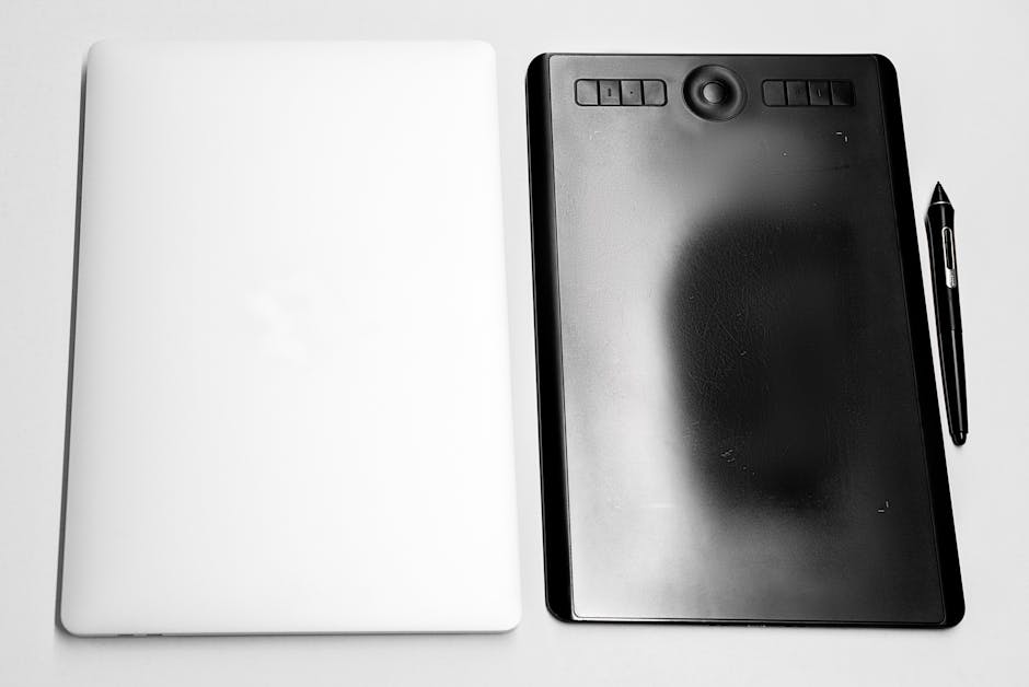 Close-up of a digital drawing tablet, stylus, and closed laptop on a white background.